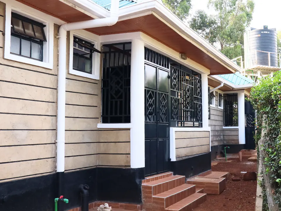 Side of a bungalow with steps up to its veranda and a hedge alongside